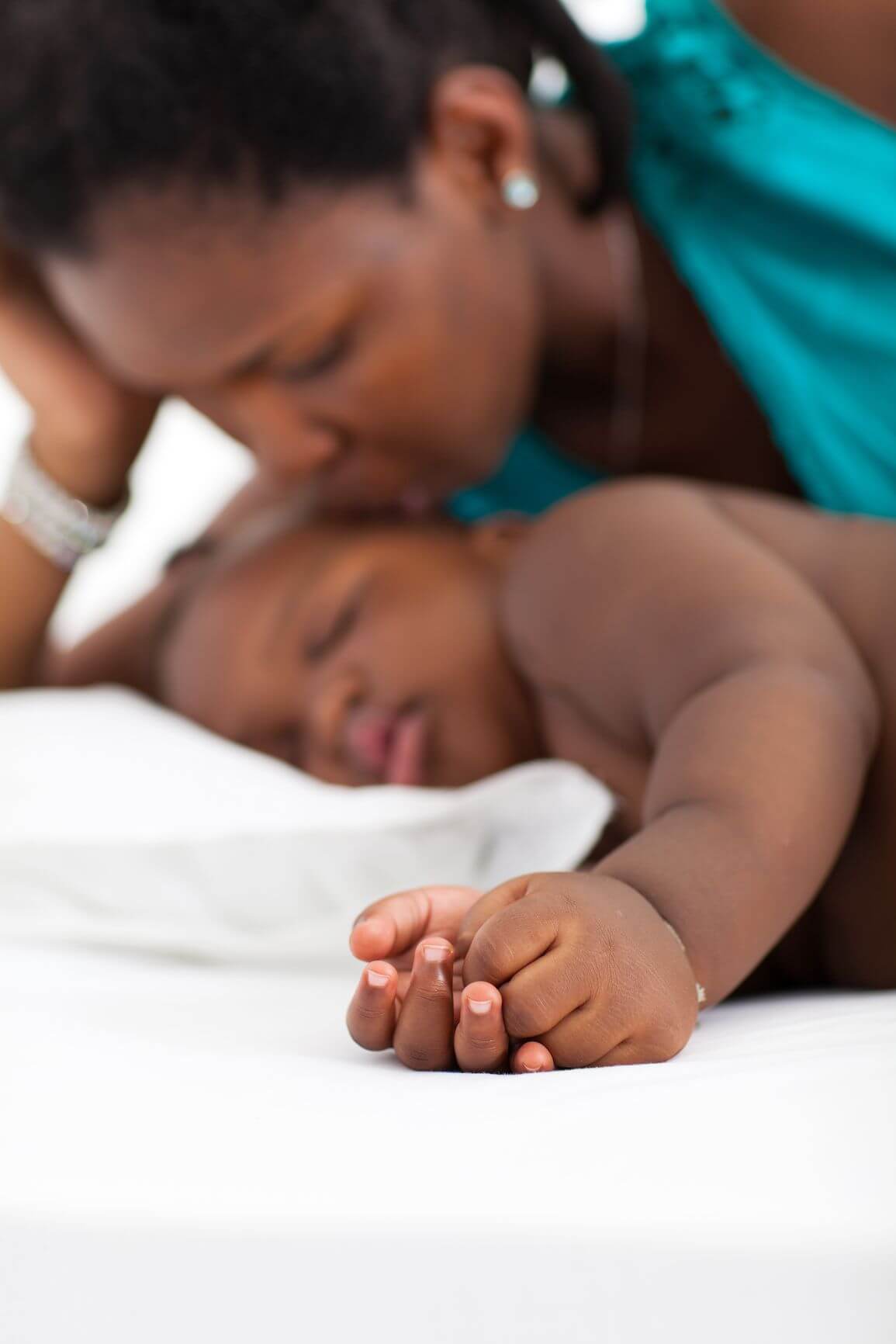 woman and her sleeping baby lying down, hands of baby are in focus